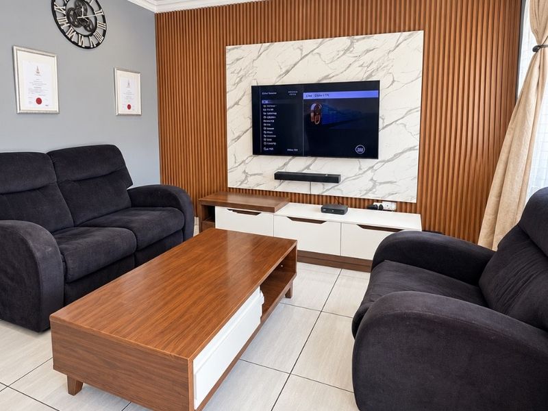 Modern living room featuring a stylish timber slat feature wall with marble-look paneling, recessed downlights, and neutral tiled flooring.