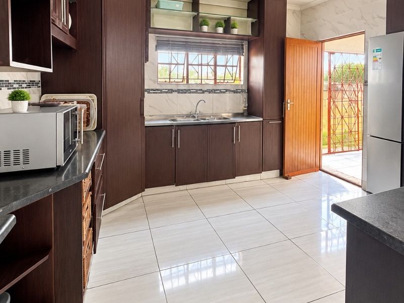 Modern kitchen featuring dark wood cabinetry, granite countertops, tiled flooring, and direct access to the exterior through a wooden door.