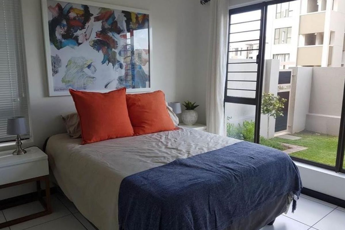 A bright bedroom featuring tiled flooring and a large sliding glass door with security bars, providing direct access to the outdoor area.