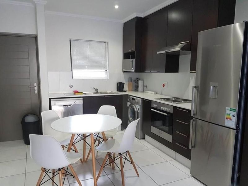 Modern open-plan kitchen featuring dark cabinetry, built-in appliances, and tiled flooring, seamlessly integrated with a dining area.