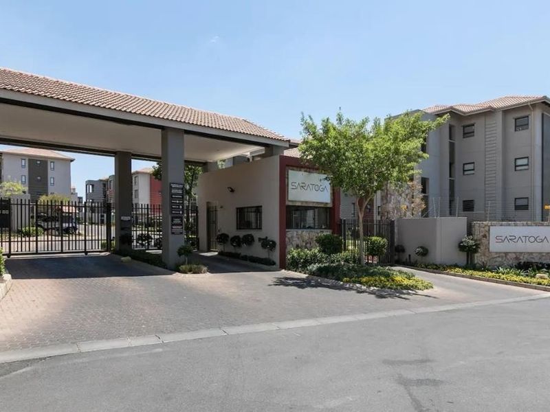 The main entrance to the Saratoga apartment complex, featuring a secure gated access point, guard house, and well-maintained landscaped surroundings.