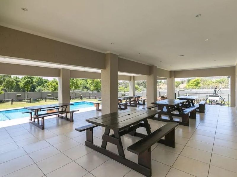 Spacious covered outdoor patio area featuring tiled flooring and recessed lighting, overlooking a private swimming pool and landscaped garden.