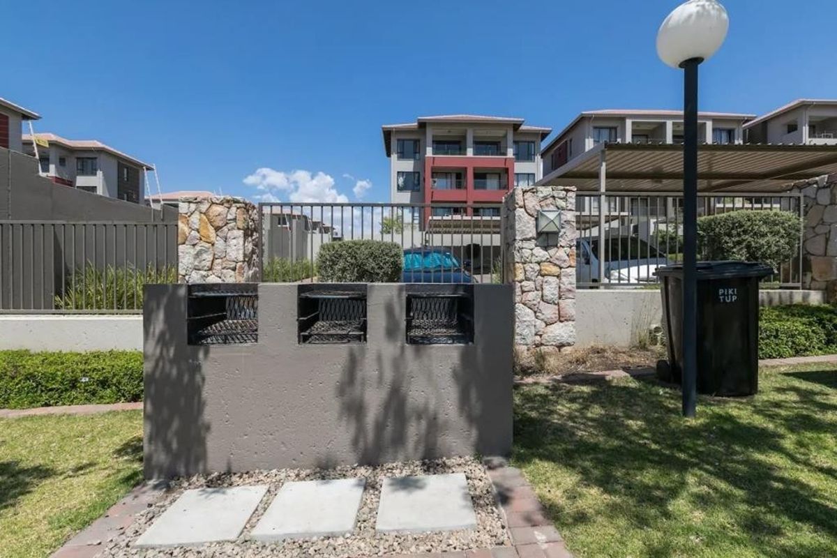 Communal outdoor area featuring a built-in triple braai station, stone-clad pillars, and paved ground, set within a well-maintained apartment complex.