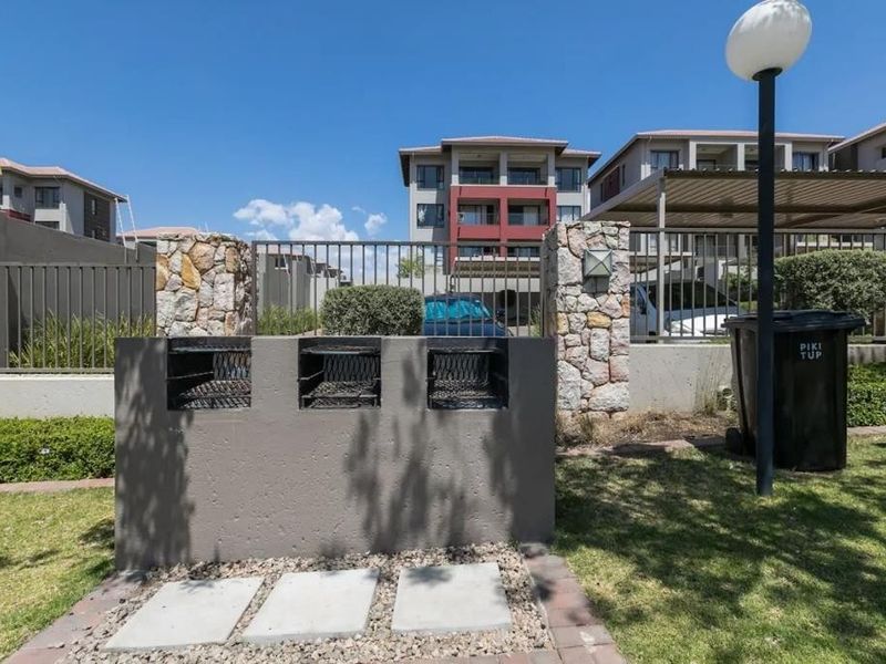 Communal outdoor area featuring a built-in triple braai station, stone-clad pillars, and paved ground, set within a well-maintained apartment complex.
