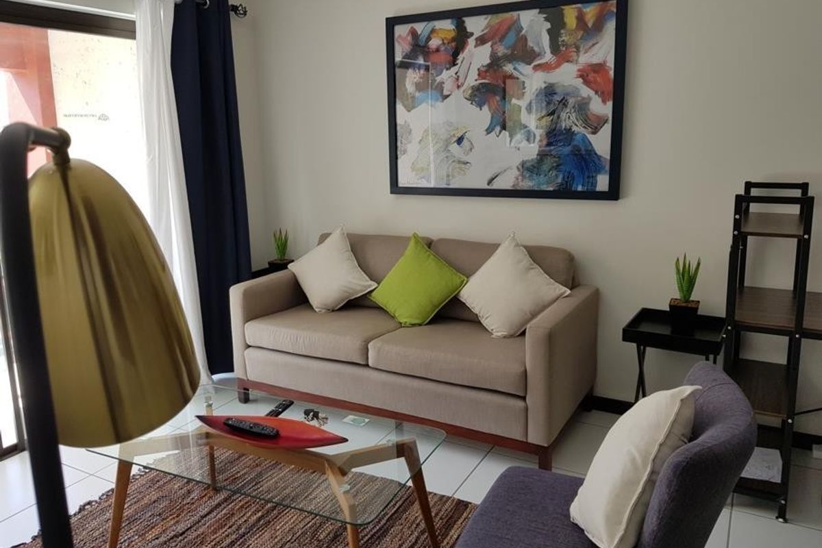 A well-lit living room featuring neutral walls, tiled flooring, and a sliding glass door providing access to the outdoor area.