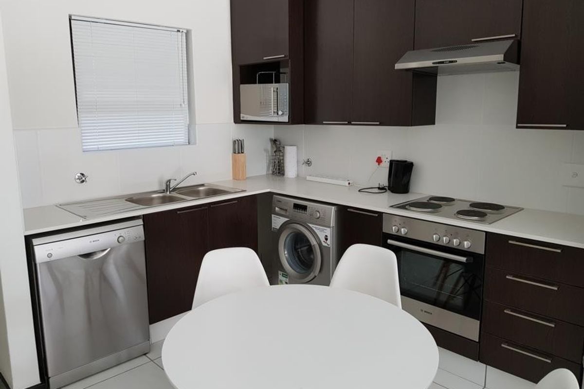 Modern kitchen featuring dark wood cabinetry, integrated appliances including a dishwasher and washing machine, and a functional layout with a built-in oven and hob.