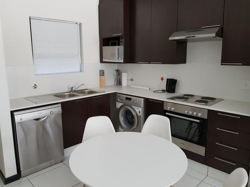 Modern kitchen featuring dark wood cabinetry, integrated appliances including a dishwasher and washing machine, and a functional layout with a built-in oven and hob.