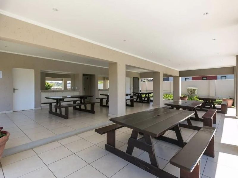 A spacious covered outdoor patio area featuring tiled flooring, structural columns, and a built-in serving counter, ideal for communal gatherings.