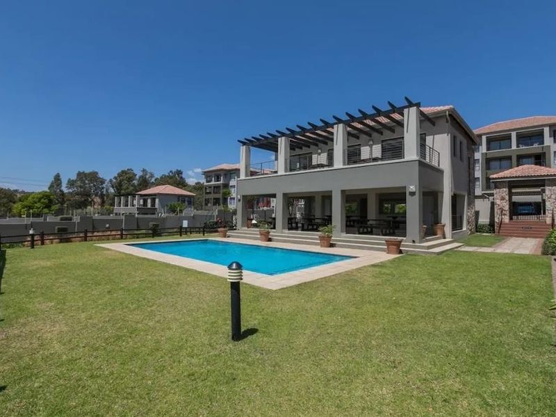 A well-maintained outdoor area featuring a swimming pool, paved surround, and a covered patio with a timber pergola, set within a landscaped garden.