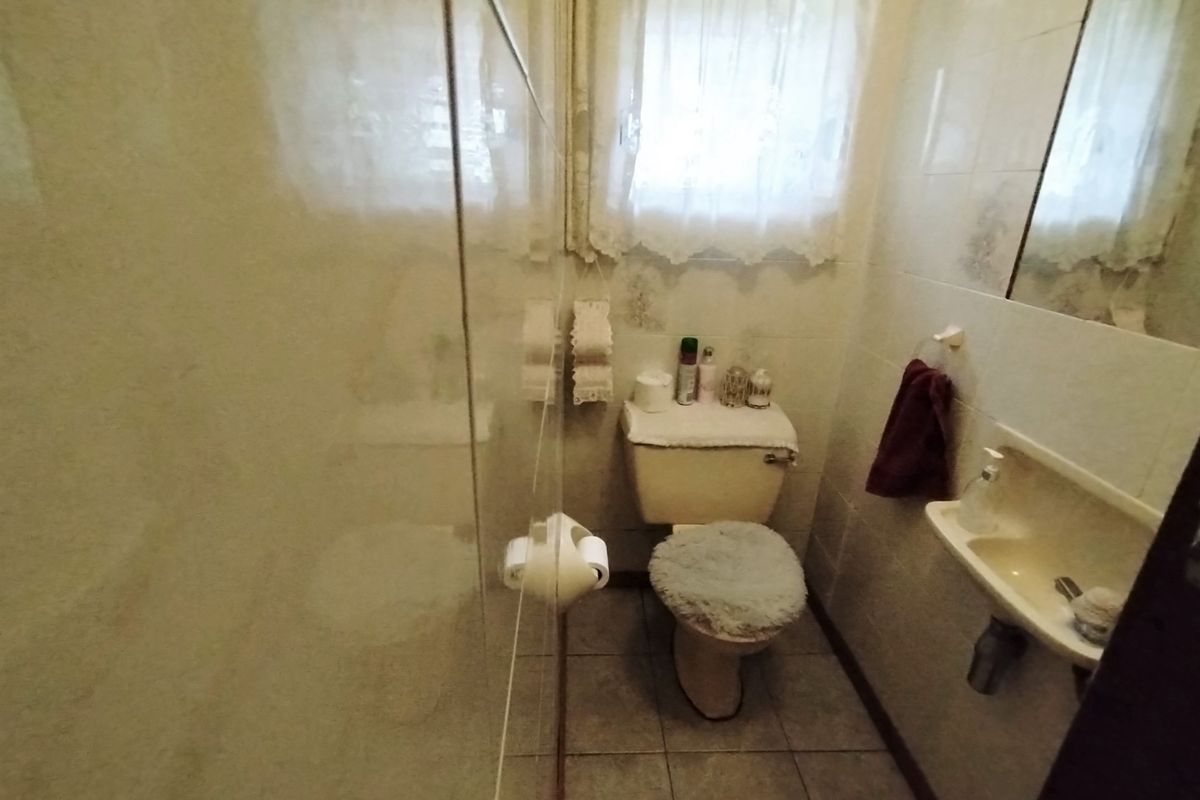 A compact bathroom featuring a toilet, wall-mounted basin, and a shower enclosure with tiled walls and flooring.
