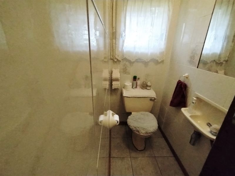 A compact bathroom featuring a toilet, wall-mounted basin, and a shower enclosure with tiled walls and flooring.