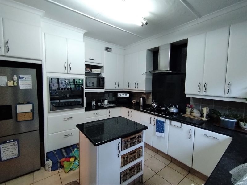 A functional kitchen featuring white cabinetry, granite countertops, a central island, and integrated appliances including an oven, microwave, and extractor fan.