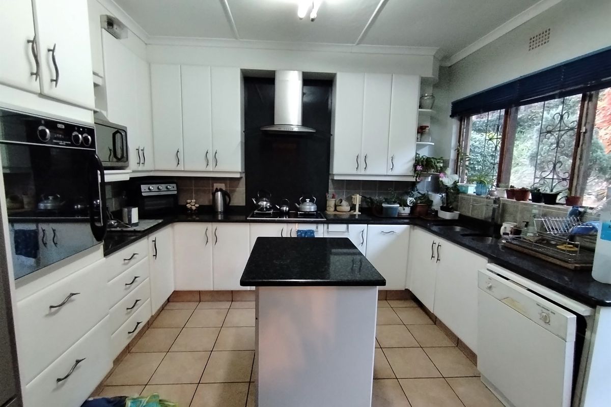 A functional kitchen featuring white cabinetry, granite countertops, a central island, built-in oven, and extractor fan with tiled flooring.