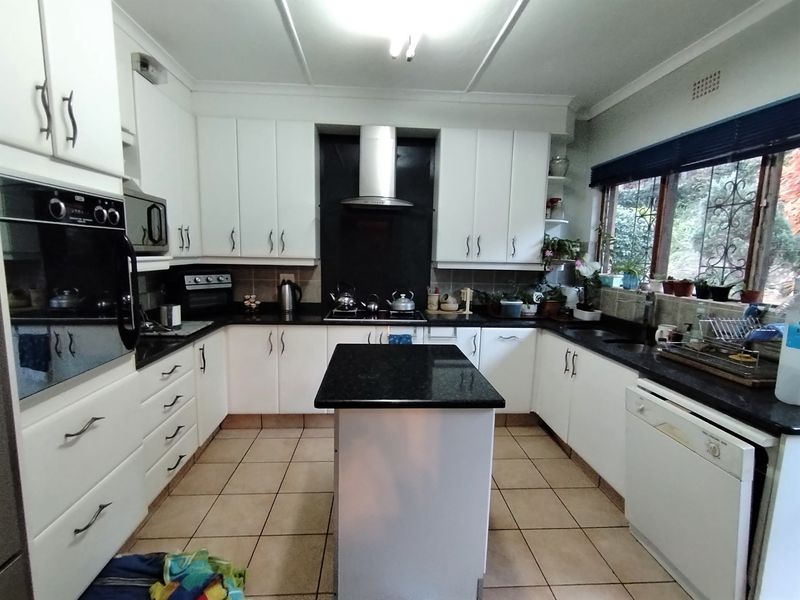 A functional kitchen featuring white cabinetry, granite countertops, a central island, built-in oven, and extractor fan with tiled flooring.
