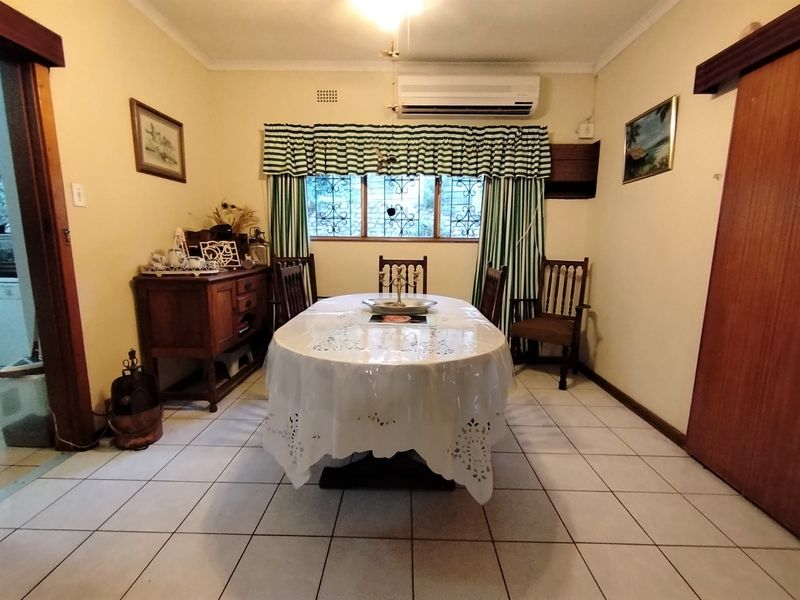 A functional dining room featuring tiled flooring, a wall-mounted air conditioning unit, and security bars on the windows.