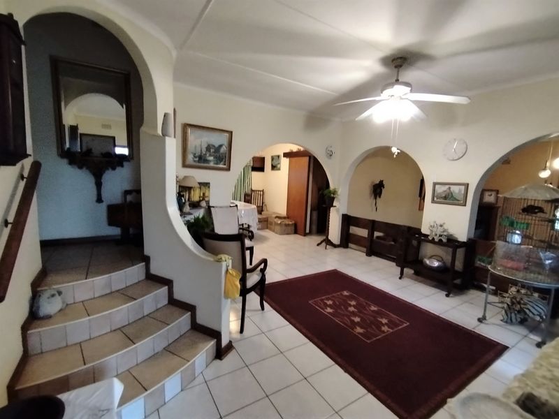 Spacious living area featuring tiled flooring, distinctive architectural archways, and a central staircase, offering a versatile layout with classic design elements.
