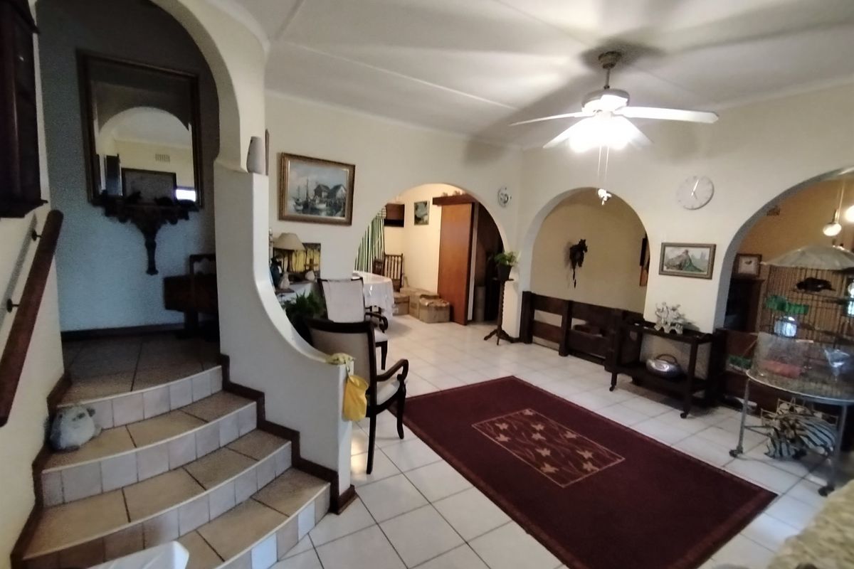 Spacious living area featuring tiled flooring, distinctive architectural archways, and a central staircase, offering a versatile layout with classic design elements.