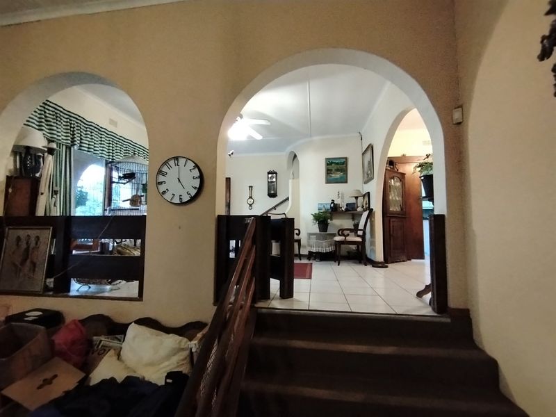 A split-level hallway featuring arched architectural openings, tiled flooring, and a wooden staircase with a balustrade leading to the upper living area.