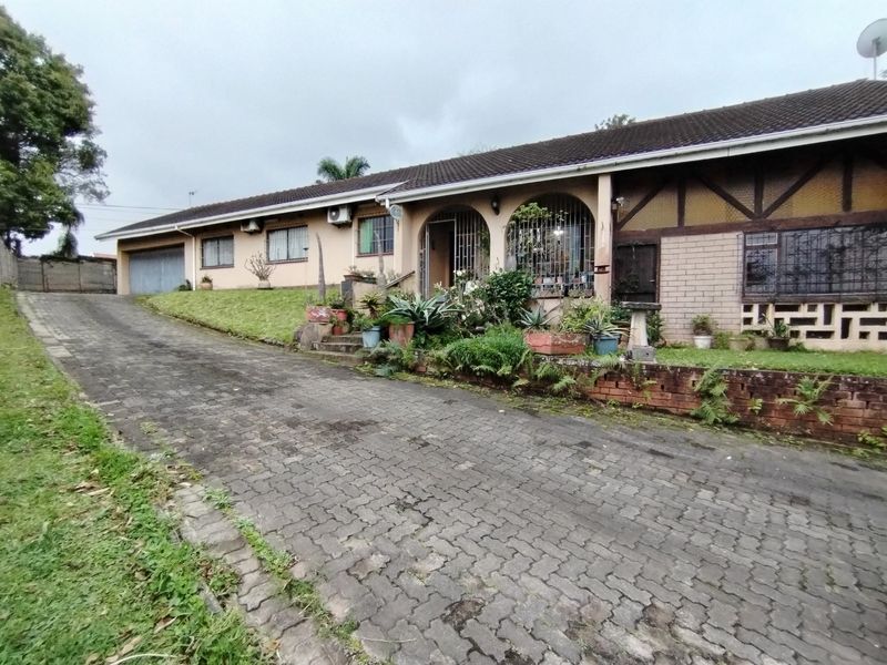 Front elevation of a single-story house featuring a long paved driveway, brick retaining wall, and security-fitted windows under a tiled roof.