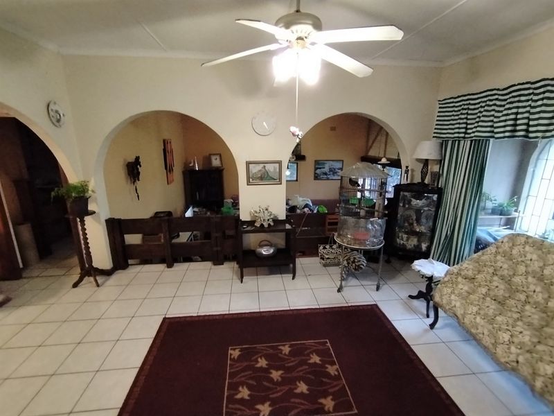 Living room featuring arched architectural details, tiled flooring, and a central ceiling fan, offering a traditional layout with potential for modernization.