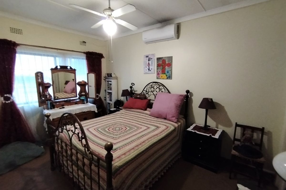 A functional bedroom featuring a ceiling fan, split-system air conditioning unit, and security burglar bars on the window.