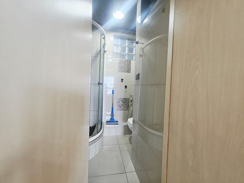A compact bathroom featuring a glass shower enclosure, tiled walls, and a glass block window for natural light.