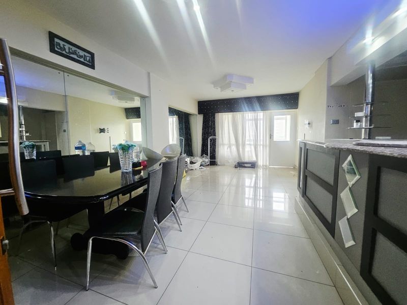 Open-plan living and dining area featuring tiled flooring, a built-in bar counter, and a large mirrored wall, leading to a balcony through sliding doors.