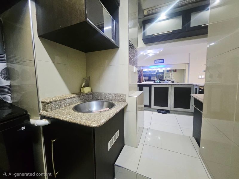 A compact kitchen area featuring granite countertops, built-in dark cabinetry, and tiled flooring, providing a functional prep space within the apartment.