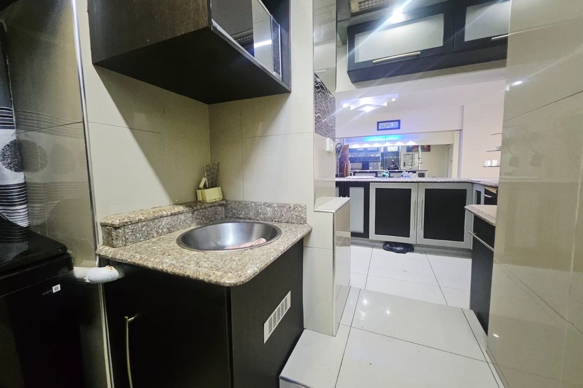A compact kitchen area featuring granite countertops, built-in dark cabinetry, and tiled flooring, providing a functional prep space within the apartment.