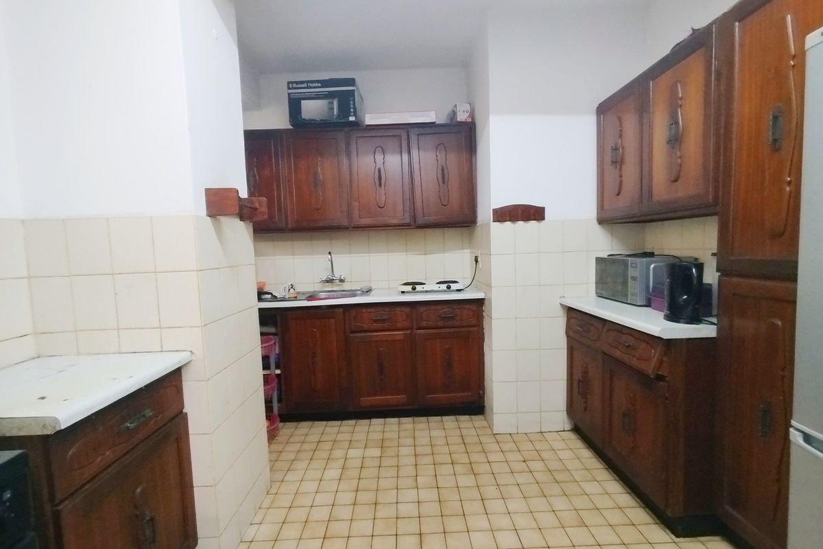 A dated kitchen featuring traditional wooden cabinetry, tiled backsplash, and tiled flooring, offering a functional layout with potential for modern renovation.