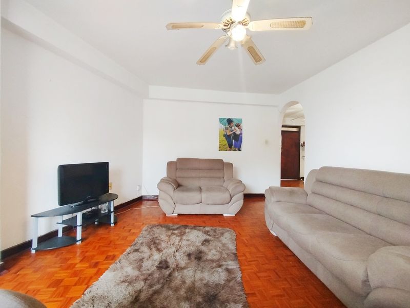 A living room featuring classic parquet flooring, a ceiling fan, and an arched entryway leading to the rest of the apartment.