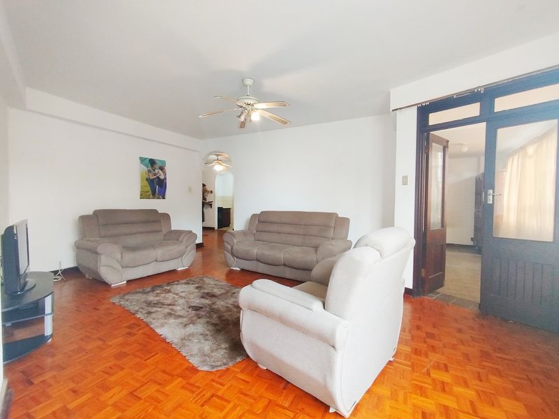A spacious living room featuring warm parquet flooring, a ceiling fan, and an arched entryway leading to adjacent living spaces.