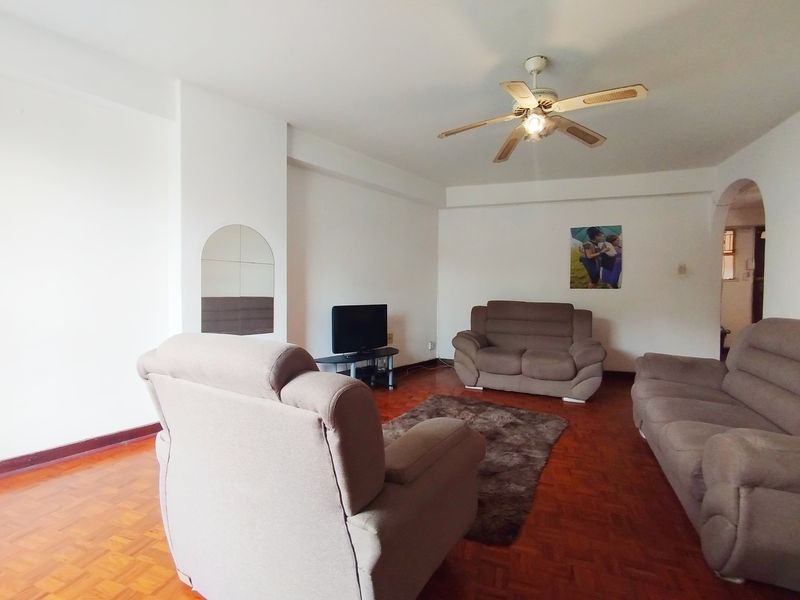 A spacious living room featuring classic parquet flooring, a ceiling fan, and an arched entryway leading to adjacent areas.