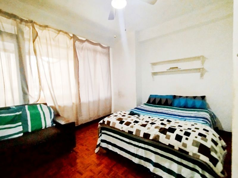 A bedroom featuring parquet flooring, a ceiling fan, and built-in wall shelving, with large windows allowing for natural light.