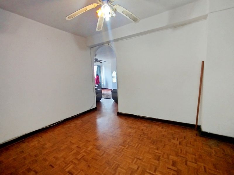 An empty living room featuring classic parquet flooring, a ceiling fan, and an arched entryway leading to an adjacent space.
