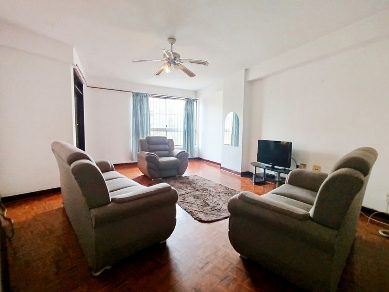 A living room featuring parquet flooring, a ceiling fan, and a window with security bars, offering a functional space with potential for modernization.