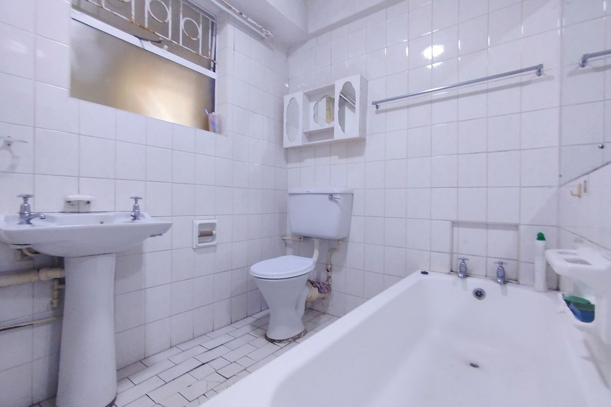 A dated bathroom featuring a pedestal basin, toilet, and bathtub with full-height wall tiling and floor tiles requiring maintenance.