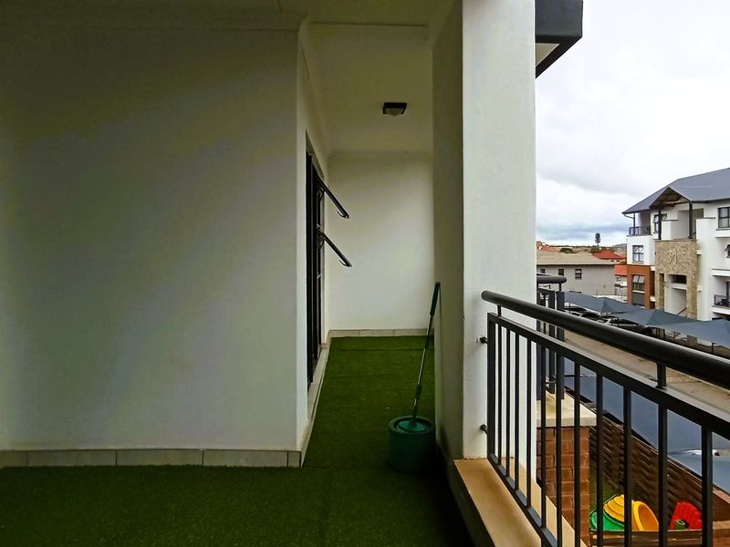 A covered balcony featuring artificial grass flooring and a metal balustrade, offering an open view of the surrounding apartment complex.
