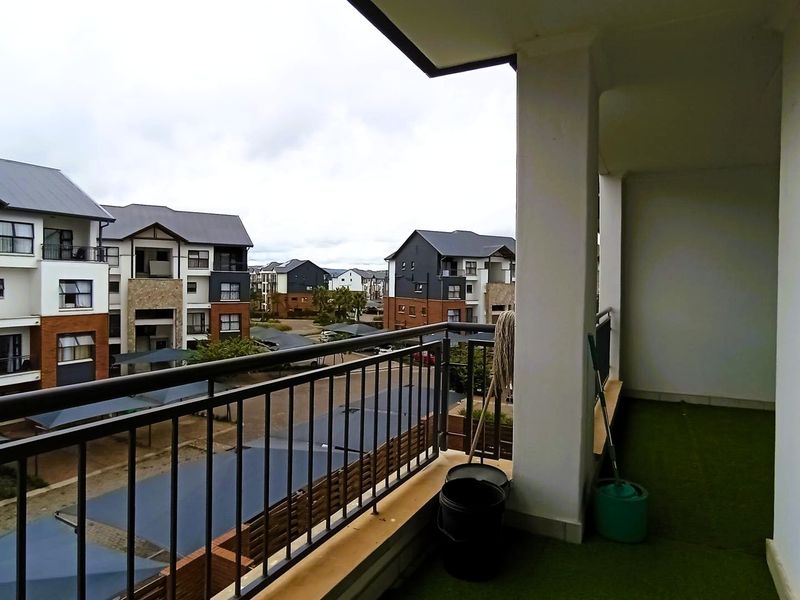 A covered balcony featuring a metal balustrade and views over the apartment complex grounds.