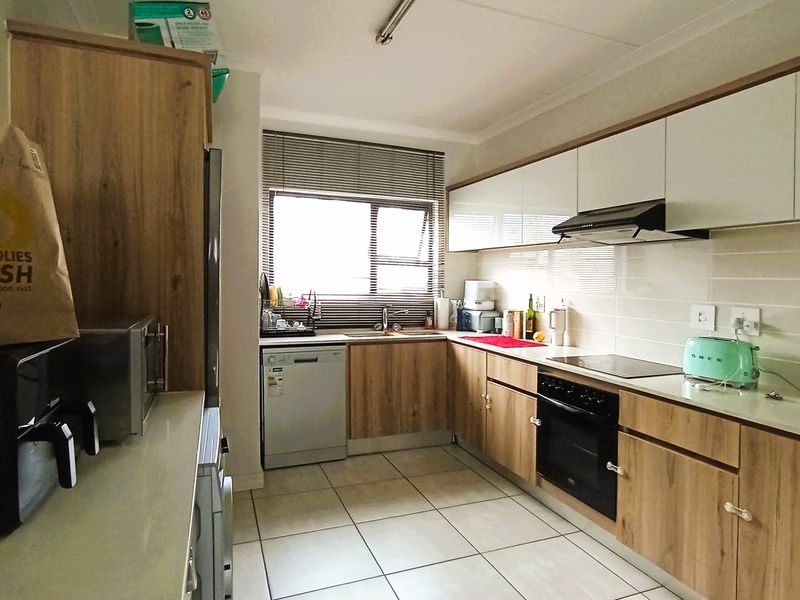 A functional kitchen featuring wood-look cabinetry, a built-in oven with hob, extractor fan, and tiled flooring, offering a clean and practical workspace.