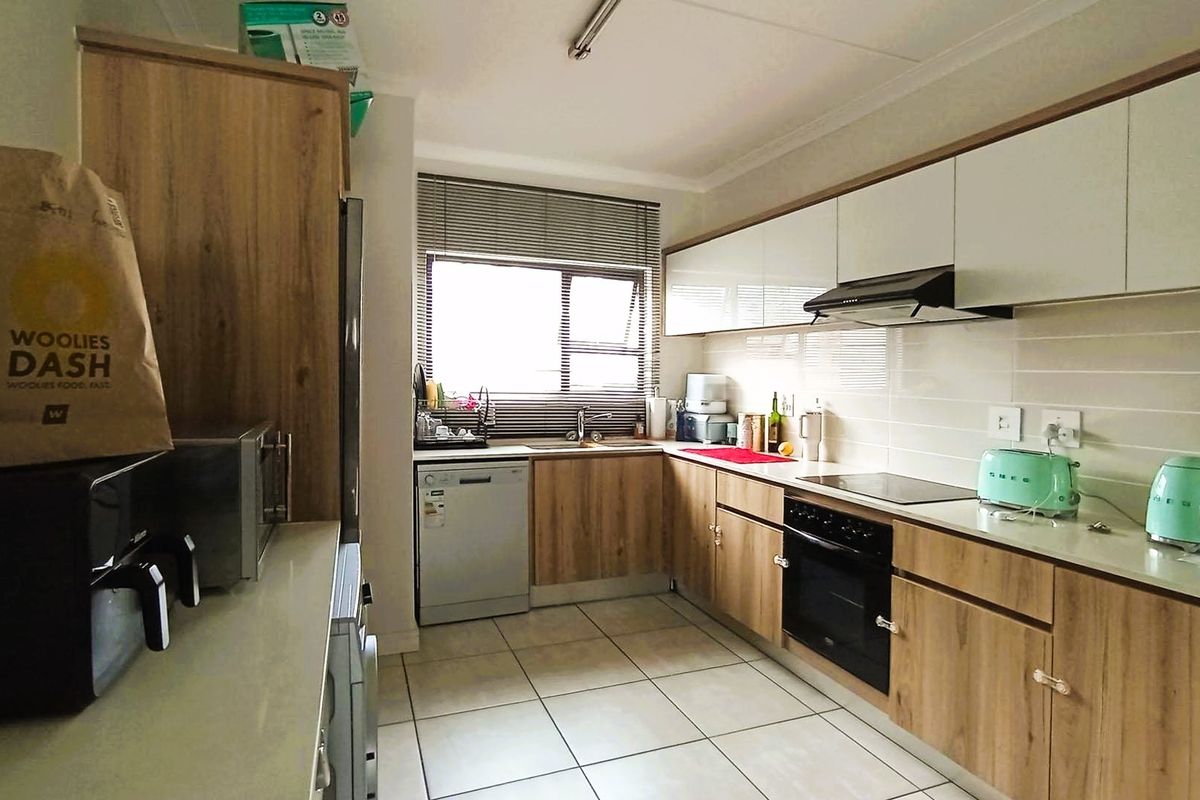 A functional kitchen featuring wood-look cabinetry, a built-in oven with hob, extractor fan, and tiled flooring, offering a clean and practical workspace.