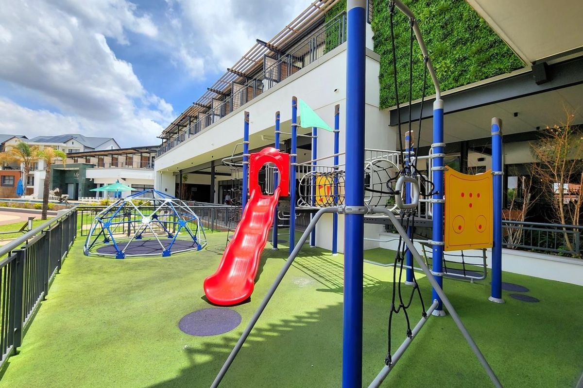 A well-maintained outdoor playground area featuring modern play equipment, artificial turf, and a vertical garden wall within an apartment complex.