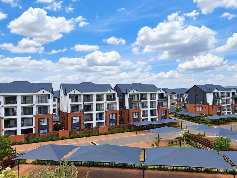 An elevated aerial view of a modern apartment complex featuring multi-story buildings with brick facades, pitched roofs, and extensive shade-covered parking areas.