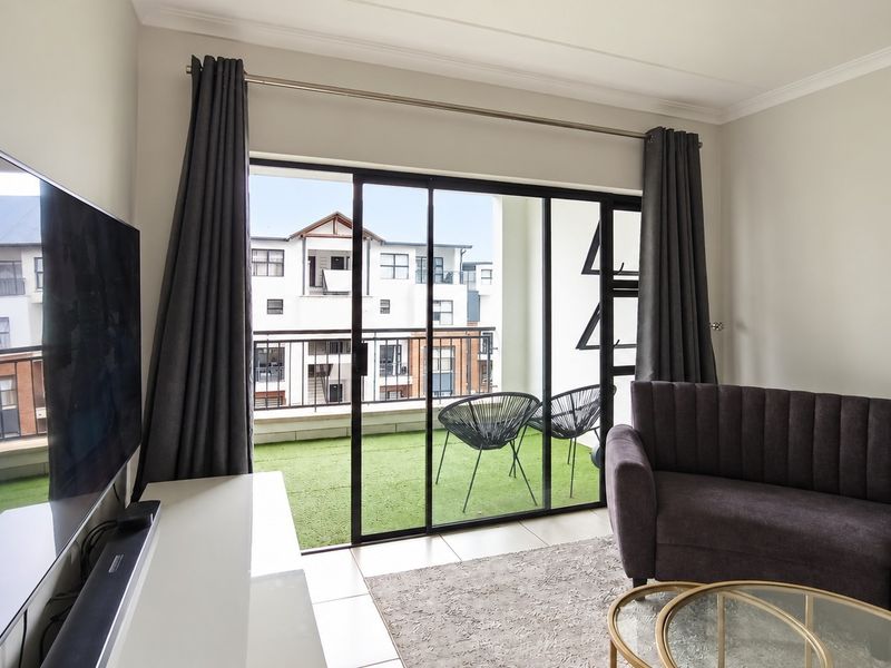 A bright living room featuring large sliding glass doors that open onto a private balcony with artificial turf.