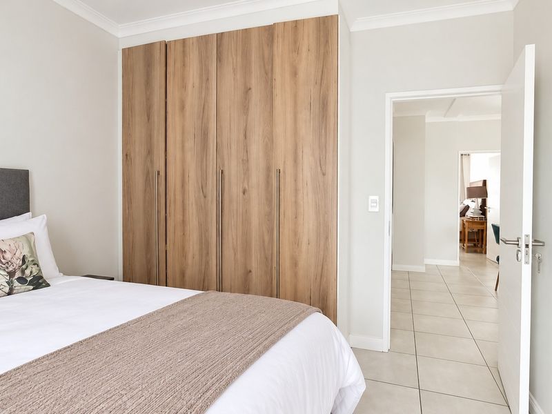 A well-maintained bedroom featuring modern wood-finish built-in cupboards, neutral tiled flooring, and clean white walls, offering a bright and contemporary living space.