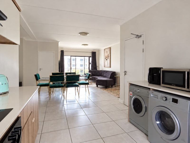 Spacious open-plan living area featuring a modern kitchen with stone countertops, integrated laundry facilities, and seamless flow to a balcony through sliding glass doors.