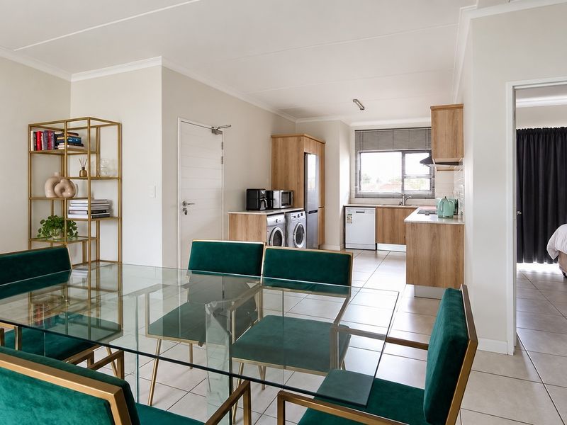 An open-plan living and dining area featuring tiled floors, neutral walls, and a functional kitchen with built-in cabinetry and integrated appliances.