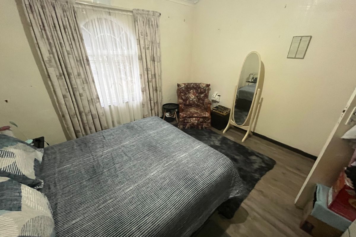 A bedroom featuring laminate flooring, an arched window with curtains, and coved ceilings, requiring some cosmetic updates to the walls and ceiling.