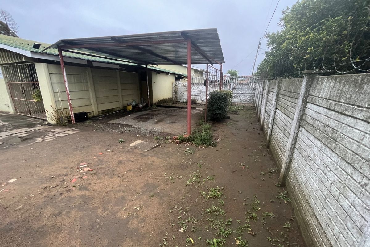 Rear exterior area featuring a metal carport structure, precast concrete boundary walls with security spikes, and an unpaved yard space.
