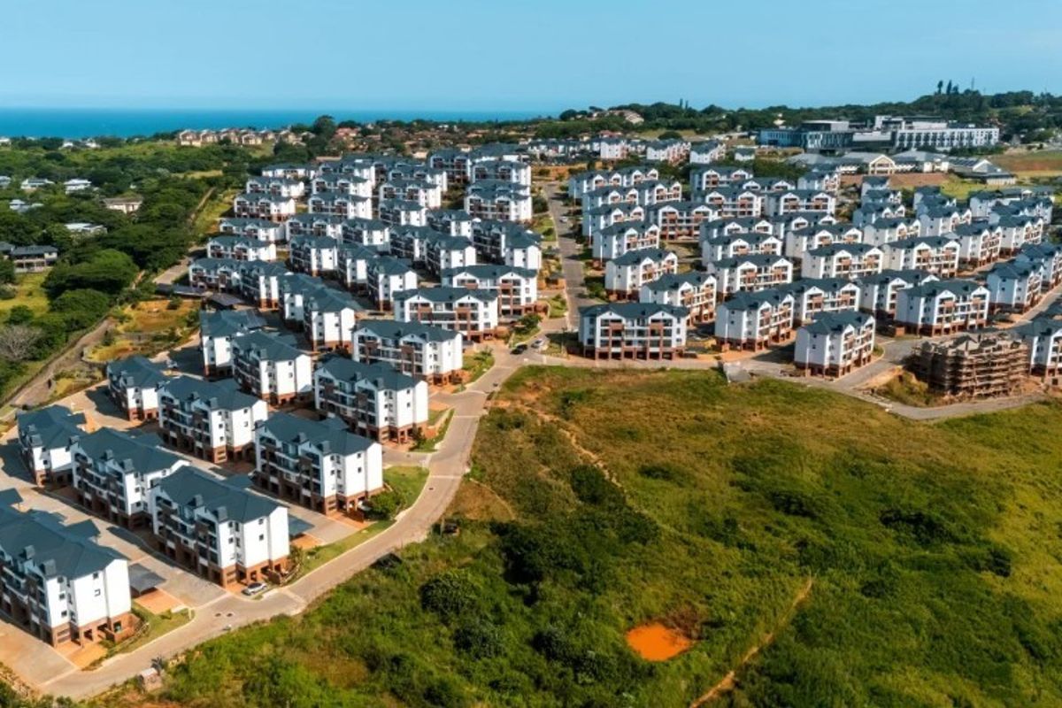 An aerial view of a large residential apartment complex featuring multiple multi-story buildings, paved internal roads, and surrounding green landscape.